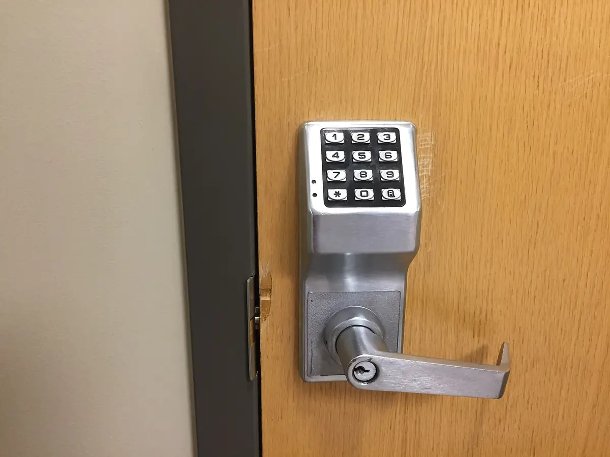 a brushed-metal keypad door lock with a lever handle on a wooden door next to a dark door frame