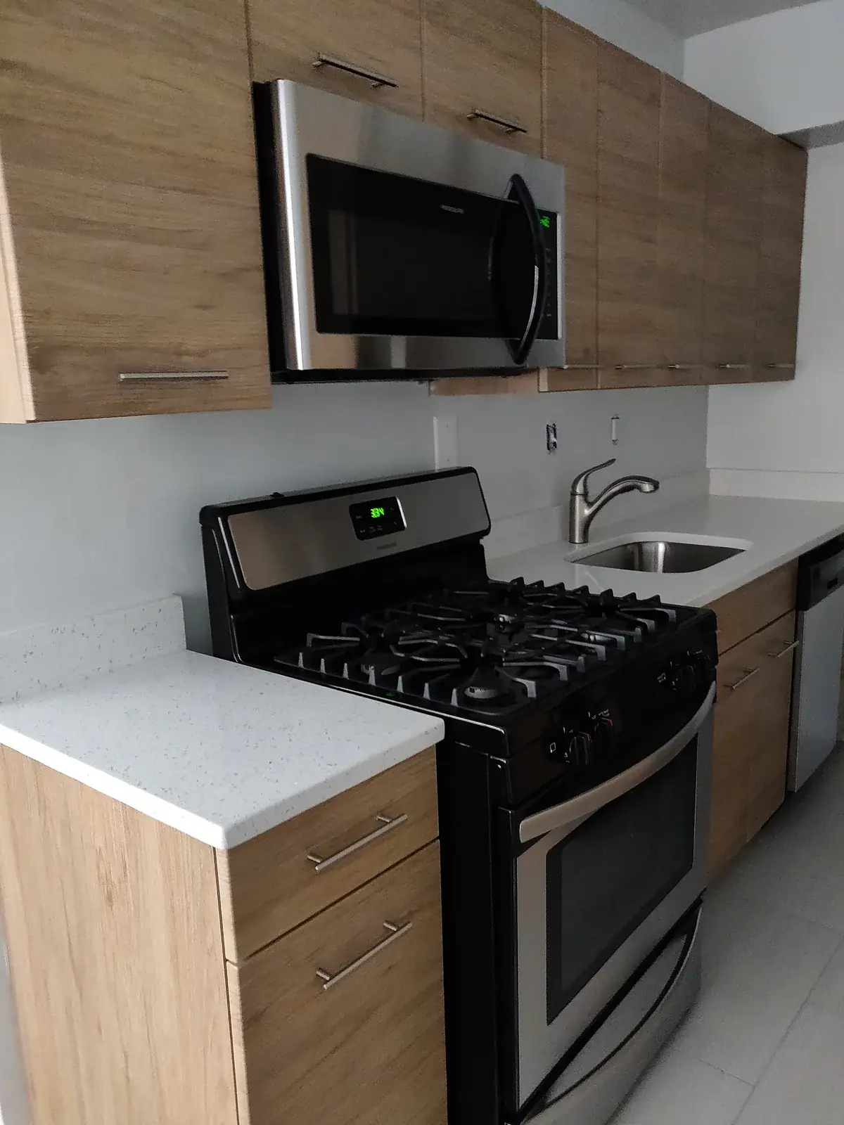 a compact kitchen with a stainless microwave mounted over a gas range between wood-look cabinets, and a sink to the side