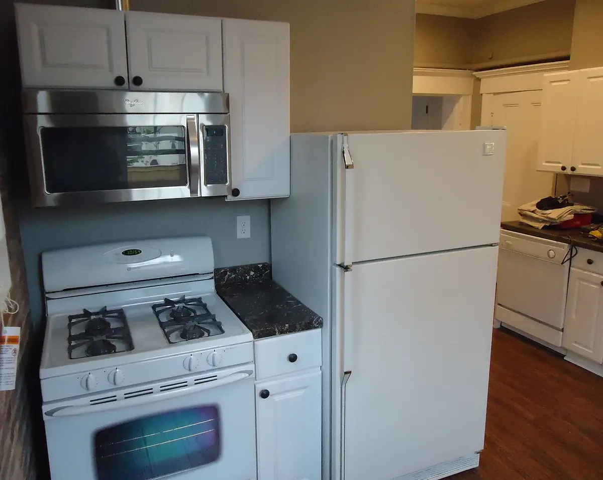 a kitchen corner with a stainless over-the-range microwave mounted under white cabinets above a white gas stove, beside a white refrigerator
