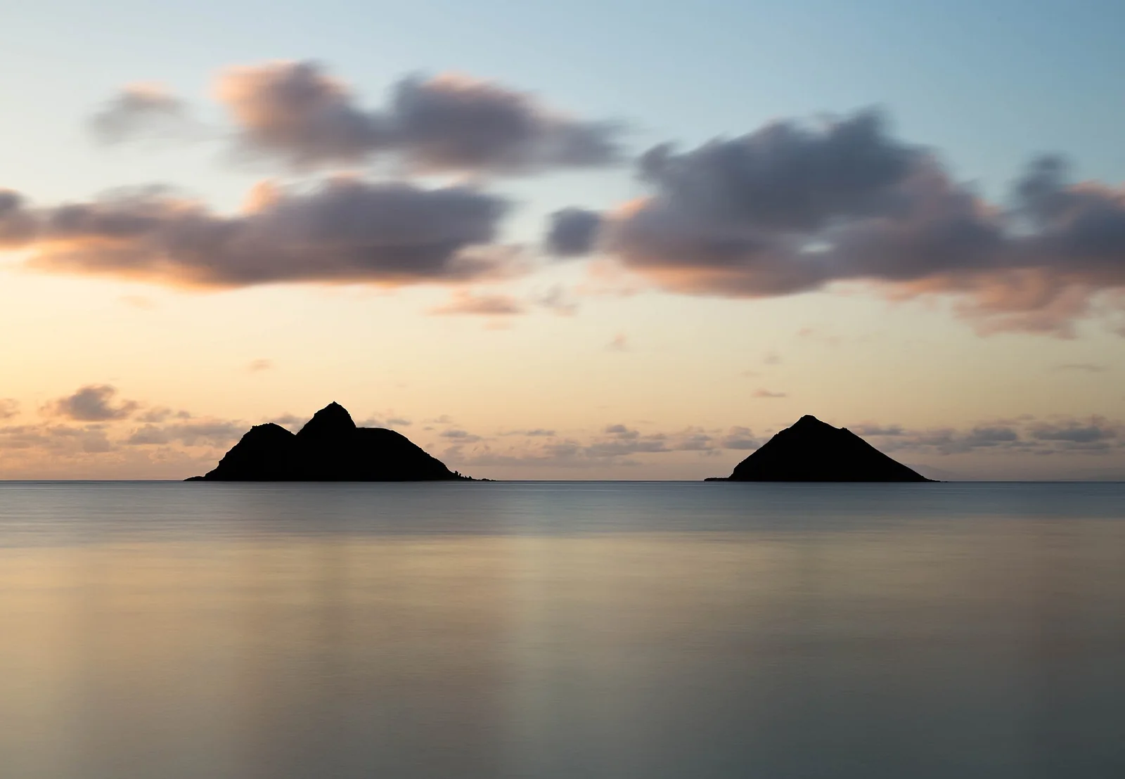 the two Mokulua islands off Lanikai Beach in Kailua, silhouetted on calm water at dusk