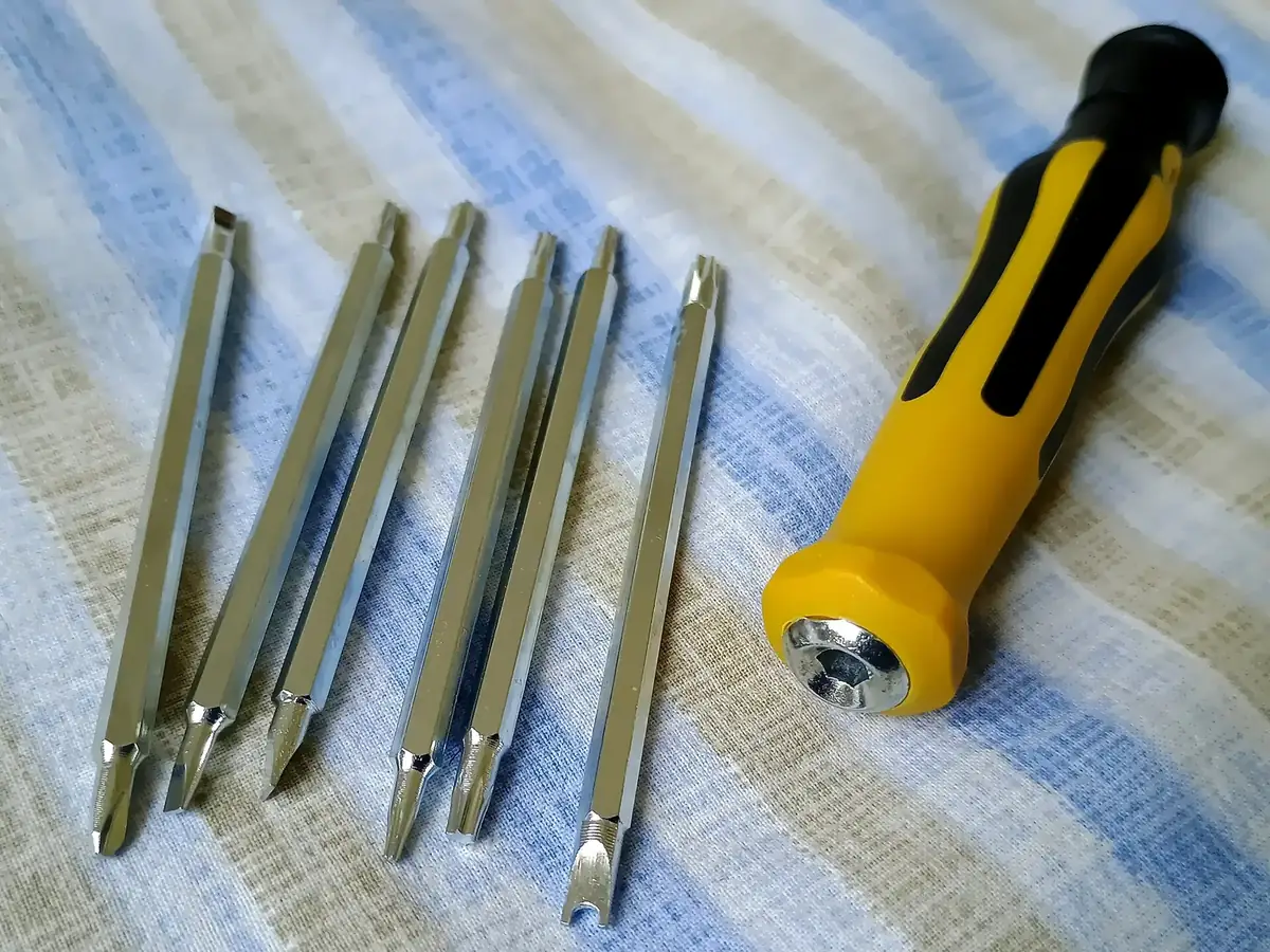 a yellow-and-black screwdriver handle beside six interchangeable steel screwdriver shafts on a striped cloth